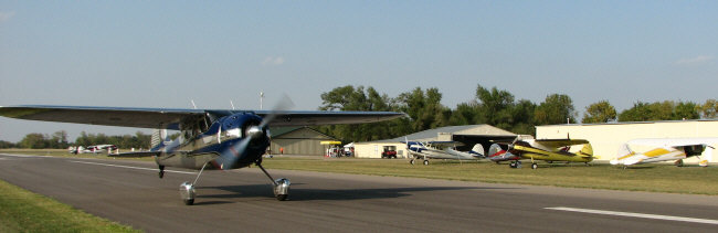 Cessna 195 -- originally this plane was the personal mount of Cessna leader Dwane Wallace.  Shown here during the 2007 International 195 Association Fly-In, taking off from Stearman Field, near Wichita, with 99-year-old former Cessna 195 test pilot Mort Brown in the pilot's seat, with his co-pilot, the plane's new owner, Cessna CEO Jack Pelton, in right seat.